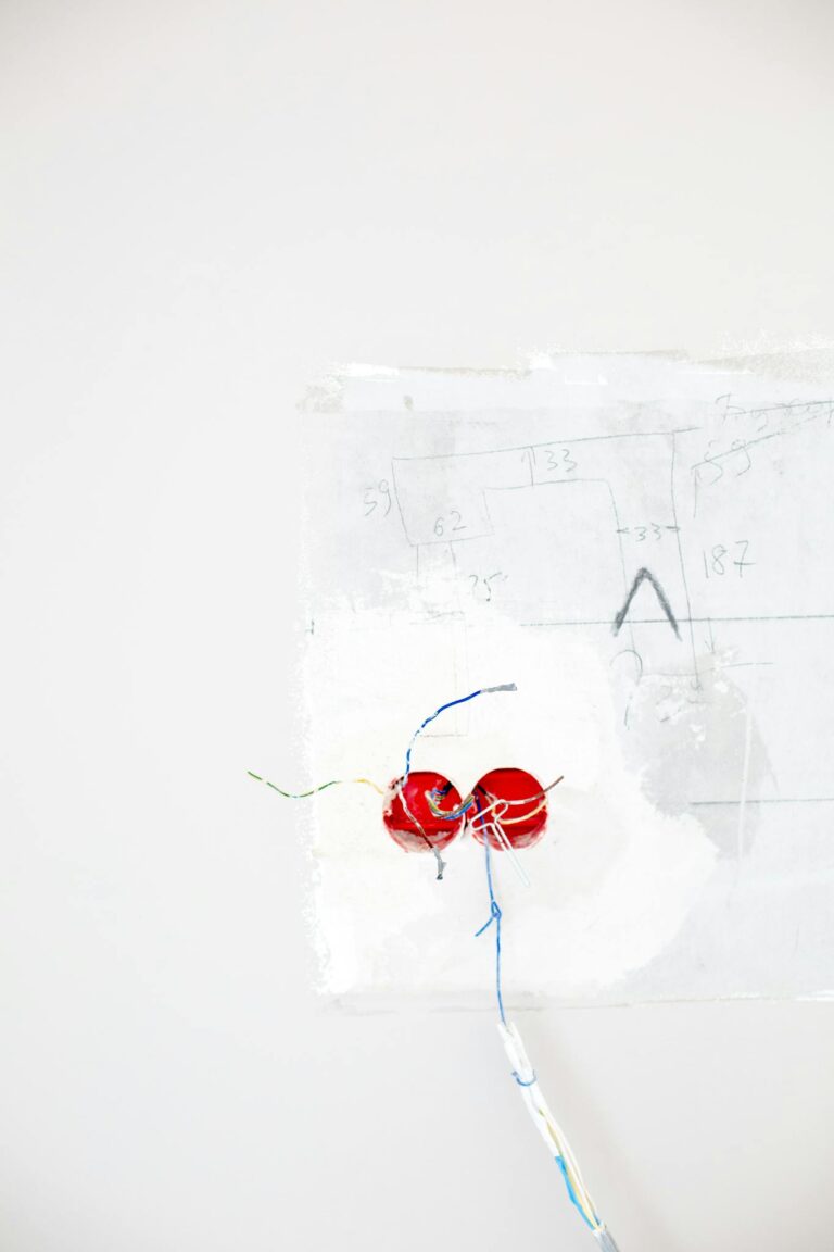 Minimalist photo of red electrical wiring emerging from a white wall background.